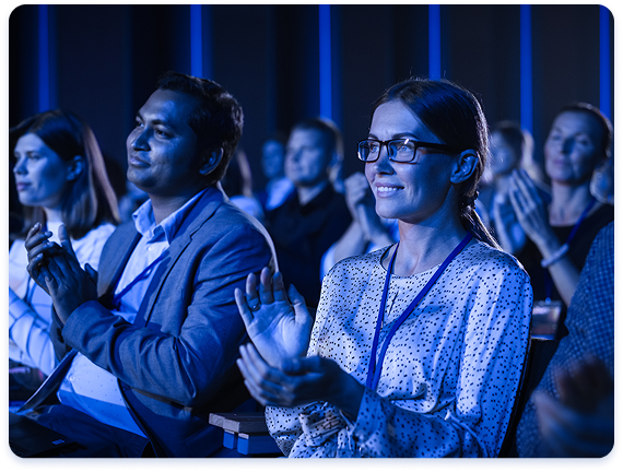 A group of conference attendees sitting in a conference room during a presentation and clapping