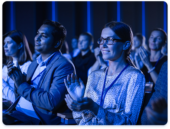 Attendees seated in a conference audience, clapping during a live presentation