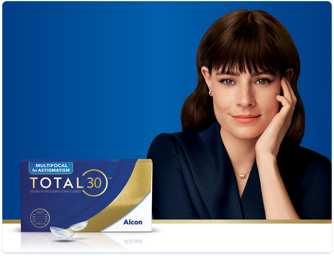 A woman sitting with her hand on her face with a box of Total30 Multifocal for Astigmatism contact lenses sitting in front of her.