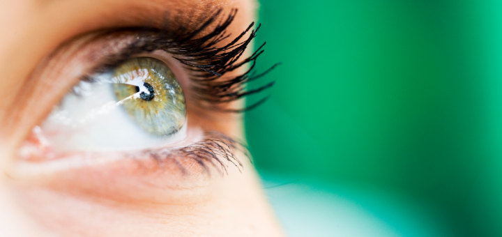 An up-close image of an eye looking upwards towards the sky, over a green background.