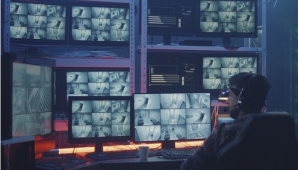 Een afbeelding van een man in een stoel met veel computerschermen voor hem.   