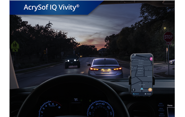 Auto op de weg in schemerlicht met telefoon op het dashboard. In de witte tekst in de linkerbovenhoek van deze afbeelding staat "AcrySof IQ Vivity". 