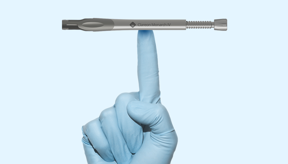 Een hand in een wegwerphandschoen met de wijsvinger omhoog wijzend. De Clareon Monarch IV Handpiece ligt horizontaal en is in balans op de wijsvinger.
