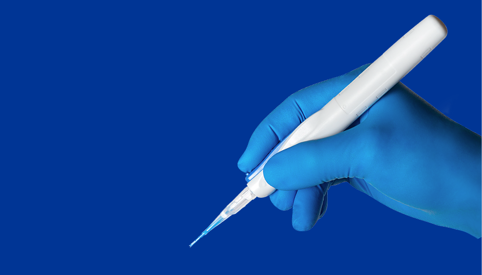 Een afbeelding van de Clareon AutonoMe Automated Preloaded Delivery System, vastgehouden door een hand in een blauwe chirurgische handschoen. De hand houdt het apparaat vast zoals men een pen zou vasthouden en verschijnt tegen een blauwe achtergrond.