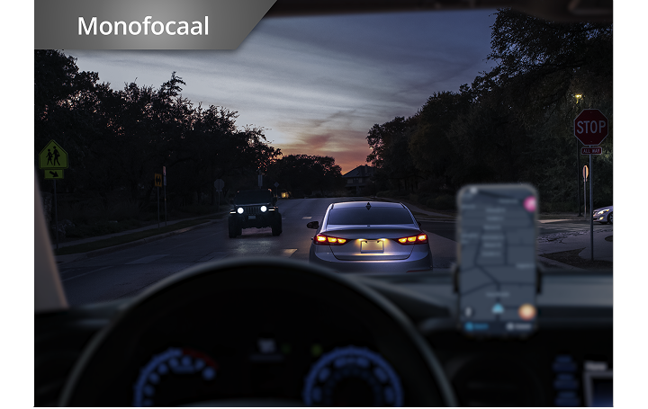 Auto op de weg in schemerlicht met telefoon op het dashboard. In de witte tekst in de linkerbovenhoek van deze afbeelding staat "Monofocaal". 
