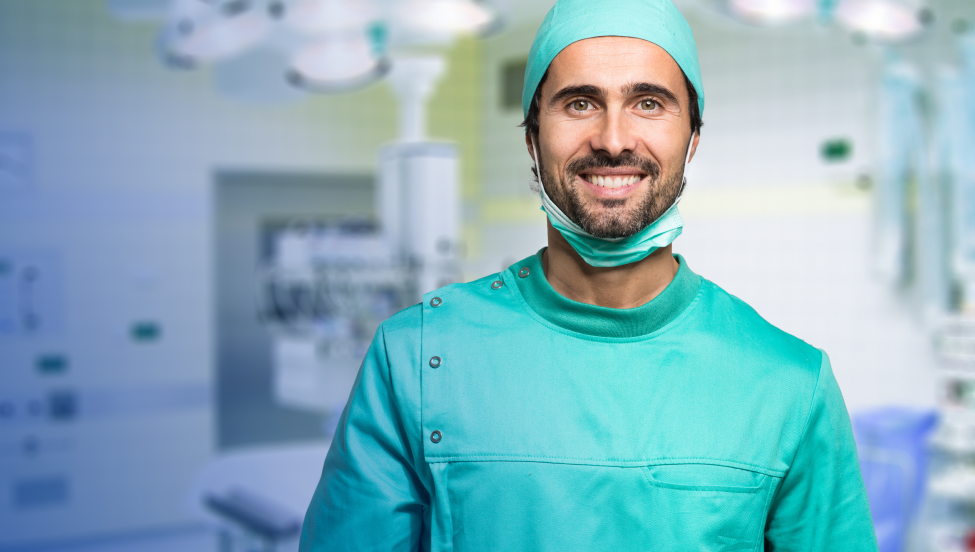 Een afbeelding van een lachende chirurg in een groenblauwe operatiejas in de operatiekamer. 