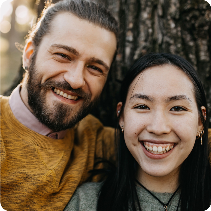 Ein lächelndes Paar lehnt an einem Baumstamm.