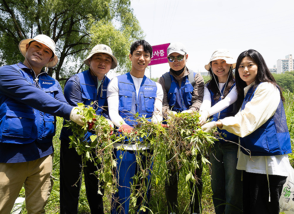 A group of people wearing blue vests and hats are planting seedlings in a field. They are smiling and working together