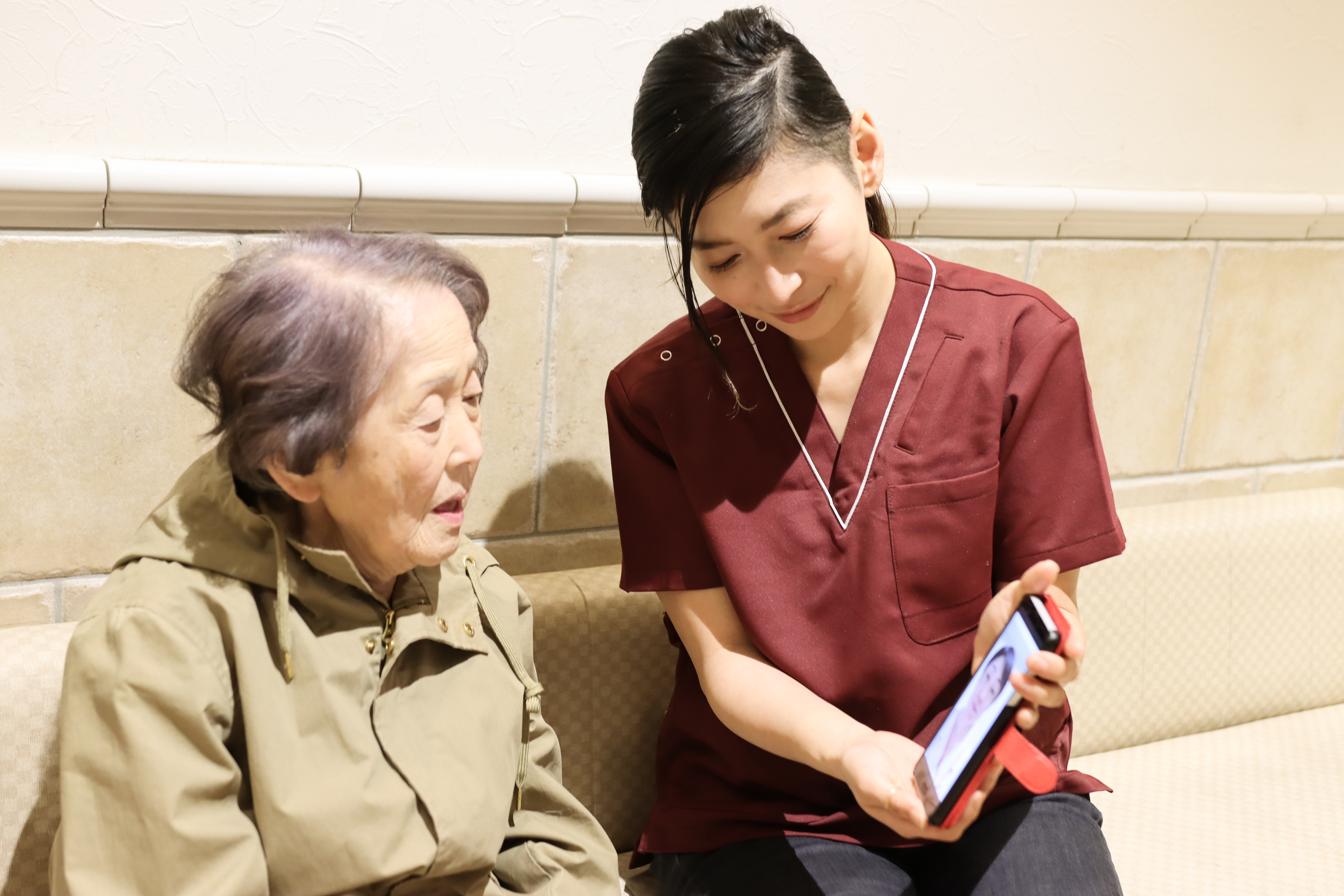 Young woman holds a phone up for an older woman who is on a video call with a medical professional