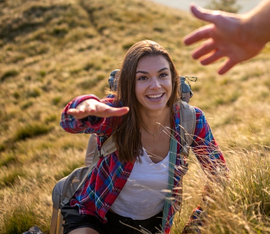  Un moment plin de bucurie și conexiune, în timp ce o femeie întinde mâna pentru ajutor într-o drumeție  intr-o zi însorită. 