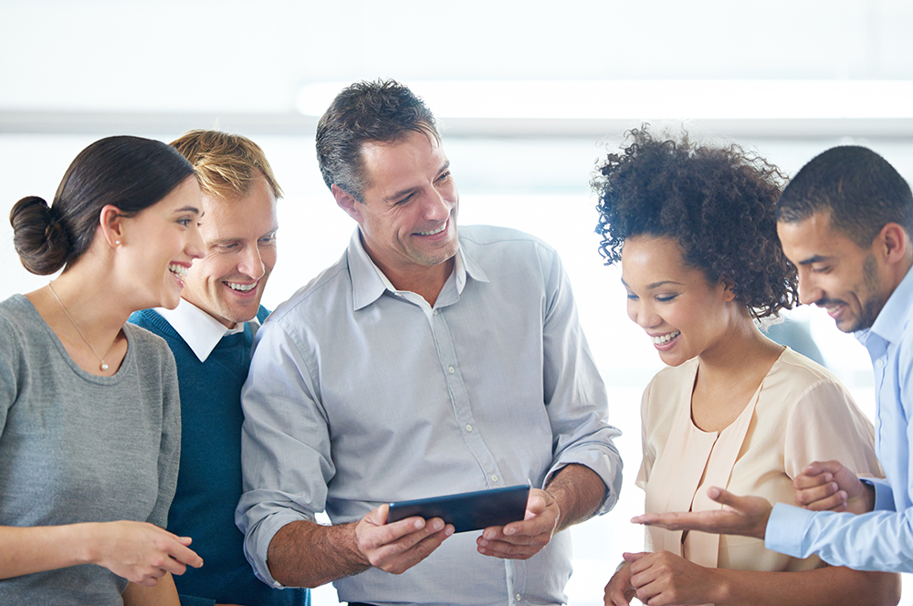 Un grupo diverso de cinco personas están de pie en círculo, mirándose entre sí y riendo. Parecen estar en una reunión informal o en un taller.