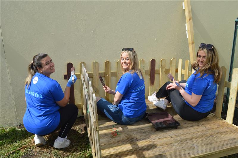 Three Alcon employees painting a fence around a wooden raised platform