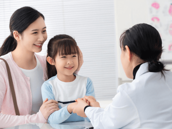 診察室で女性医師と話す笑顔の母娘。診察中、子どもは嬉しそうにくつろいでいる。