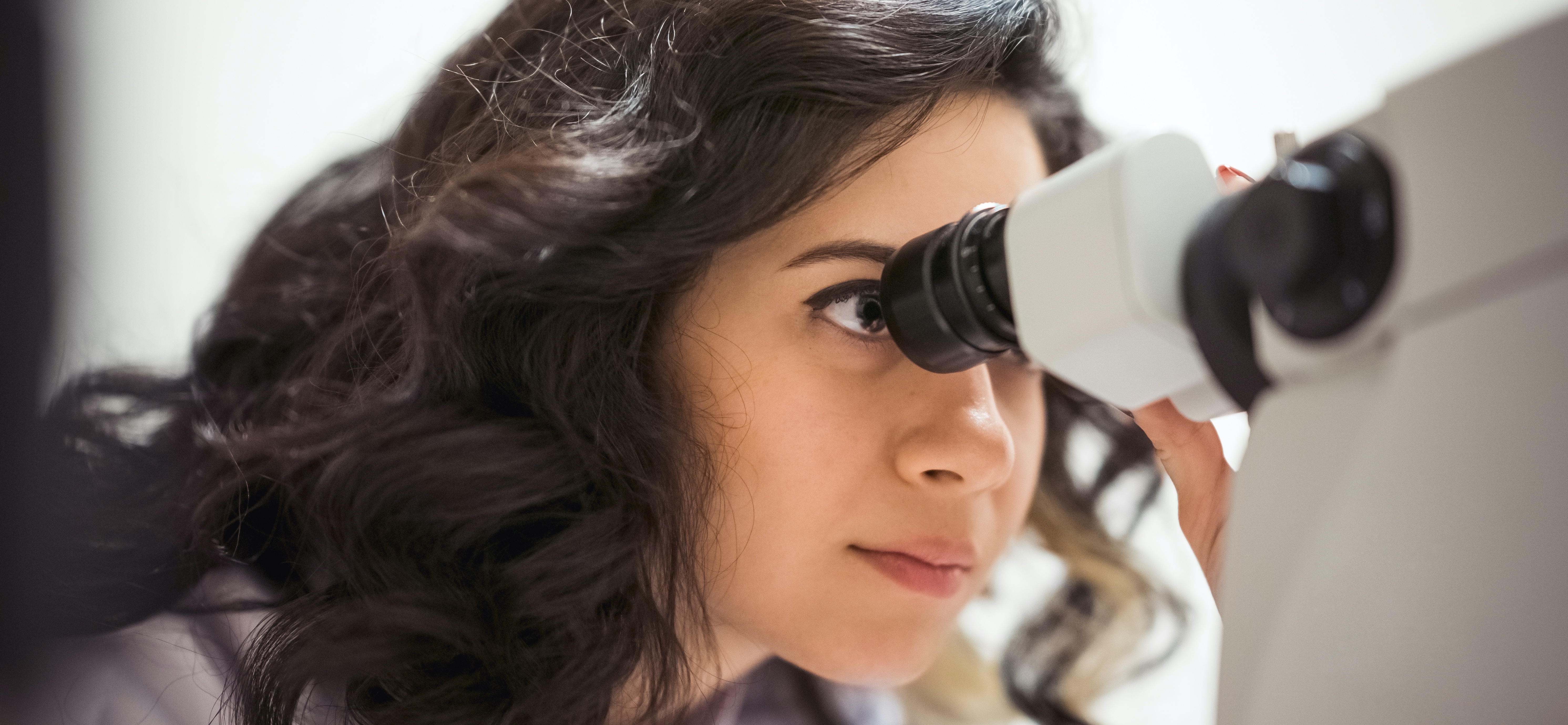 Close-up of female scientist looking into a microscope.
