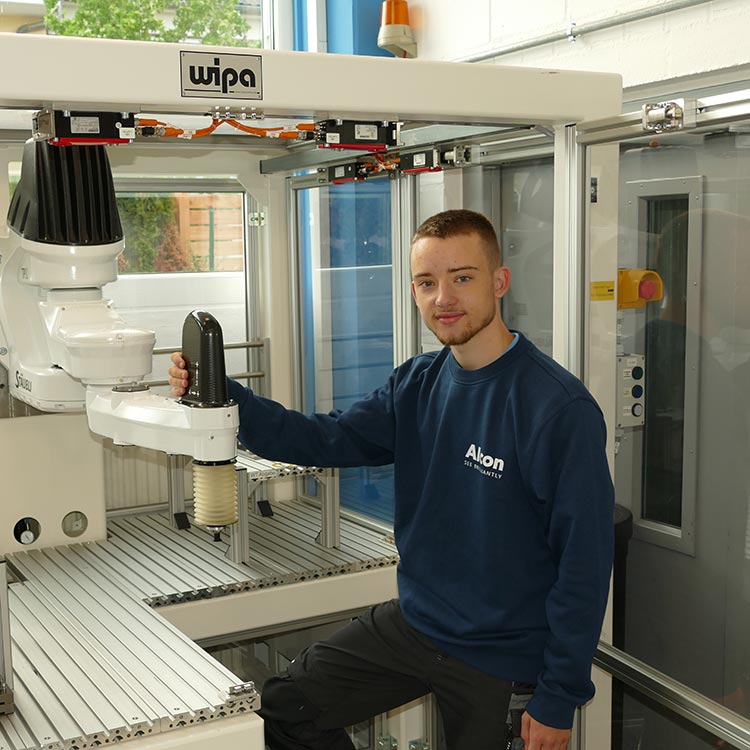 Azubi bei Alcon neben einer Robotermaschine in einer modernen Ausbildungsstätte.