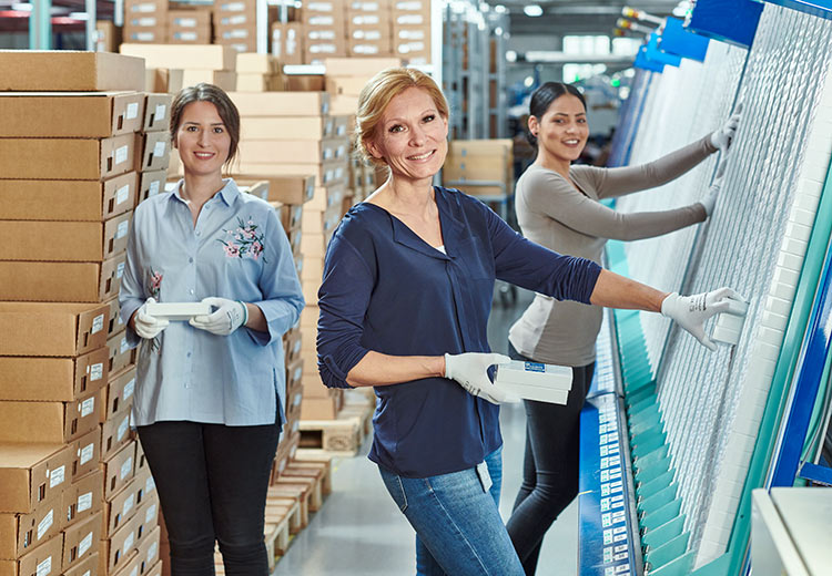 Drei Frauen arbeiten in einem Lager, handhaben verpackte Materialien und organisieren die Lagerung mit einem Lächeln.