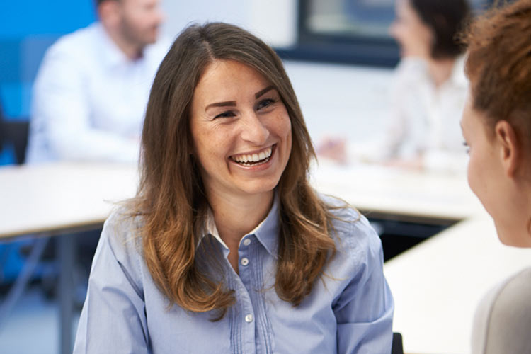 Lächelnde Frau im blauen Hemd im freundlichen Gespräch während eines Meetings in einer hellen Büroumgebung.