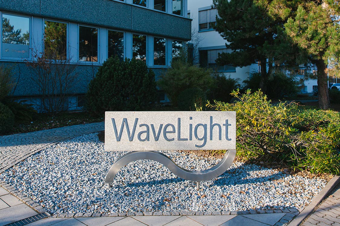 WaveLight Firmenschild vor dem Bürogebäude, umgeben von Begrünung.