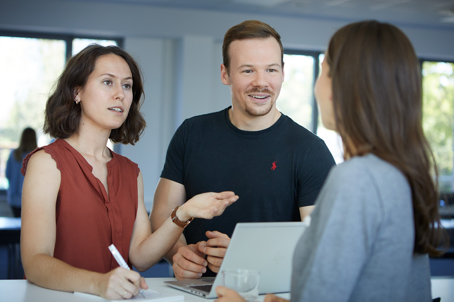 Drei junge Berufstätige diskutieren an einem Laptop in einer hellen Büroumgebung.