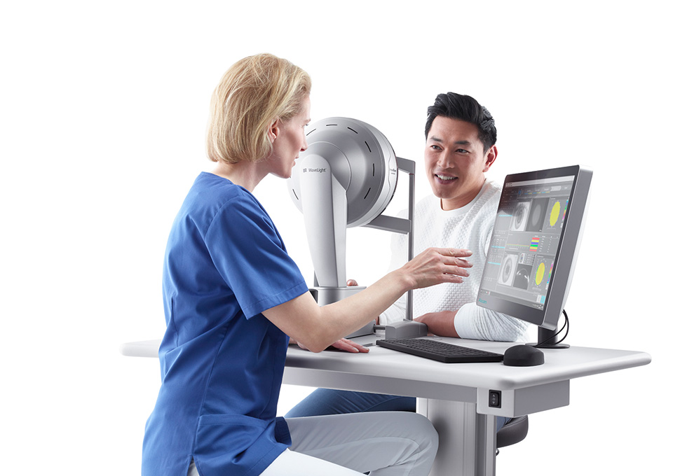 Medizinische Fachkraft verwendet ein WaveLight-Diagnosegerät und Computersoftware, um eine Augenuntersuchung bei einem lächelnden Patienten durchzuführen.