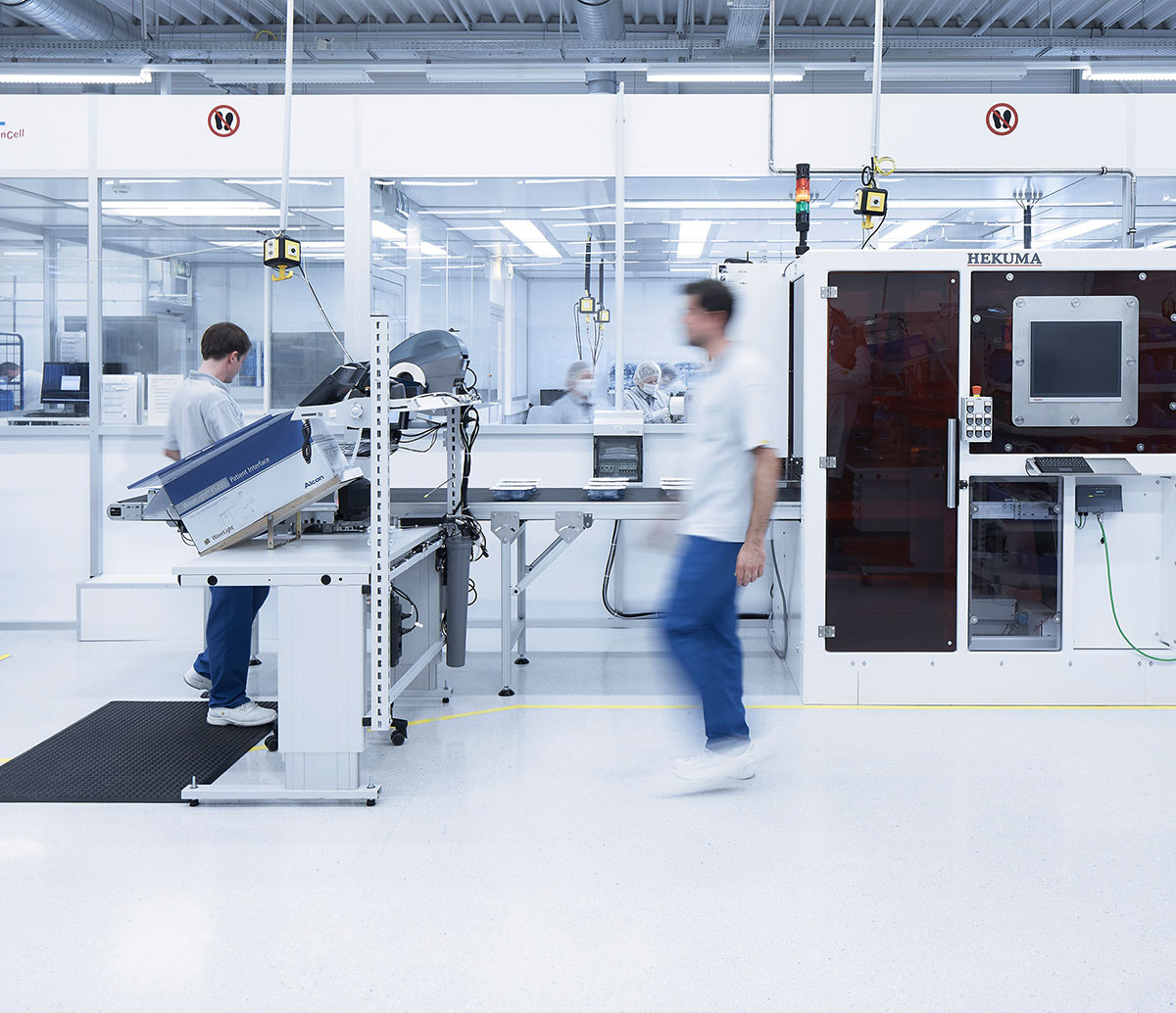 "Mitarbeiter arbeiten in einem Produktionsbereich bei Alcon mit automatisierten Maschinen."