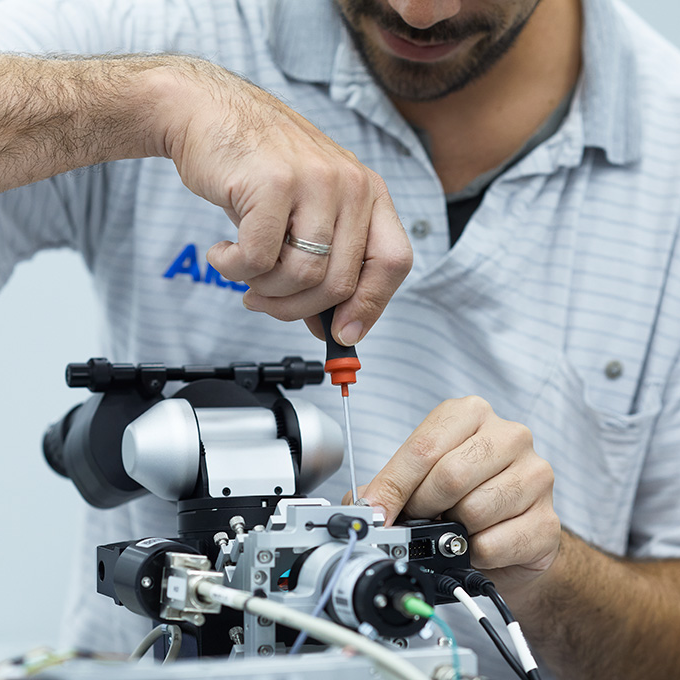 Techniker verwendet einen Schraubendreher, um Komponenten an einem präzisen optischen Gerät einzustellen.
