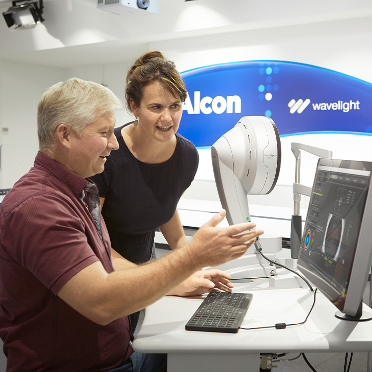 Zwei Fachleute arbeiten mit einem WaveLight Diagnosesystem und betrachten Augenscan-Ergebnisse auf einem Computerbildschirm in einer Alcon Einrichtung.