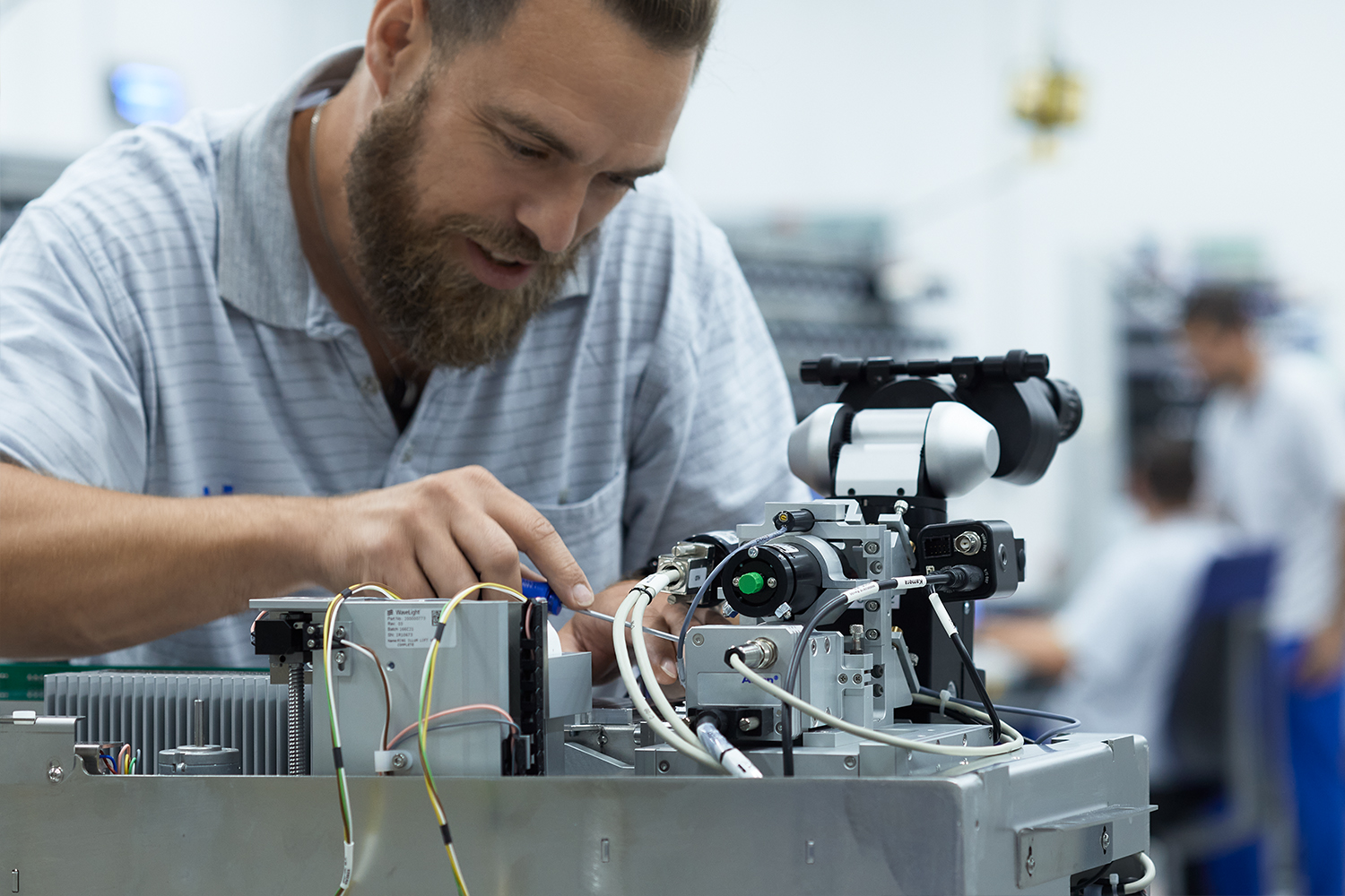 Techniker arbeitet am Zusammenbau und Testen einer komplexen Maschine mit Kabeln und optischen Komponenten.