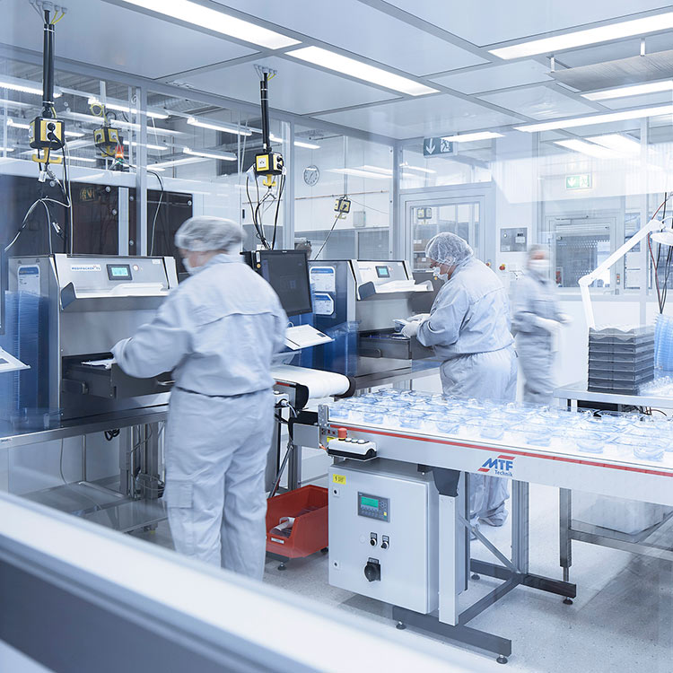 Mitarbeiter in Schutzkleidung bedienen automatisierte Maschinen in einer Reinraum-Produktionsanlage mit Verpackungsanlagen.