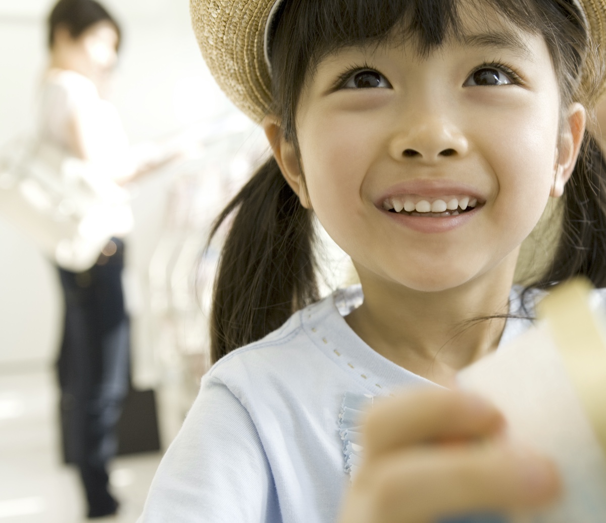  Маленькая девочка широко улыбается и держит в руке недоеденный рожок мороженого. На ней соломенная шляпа и голубая футболка. 