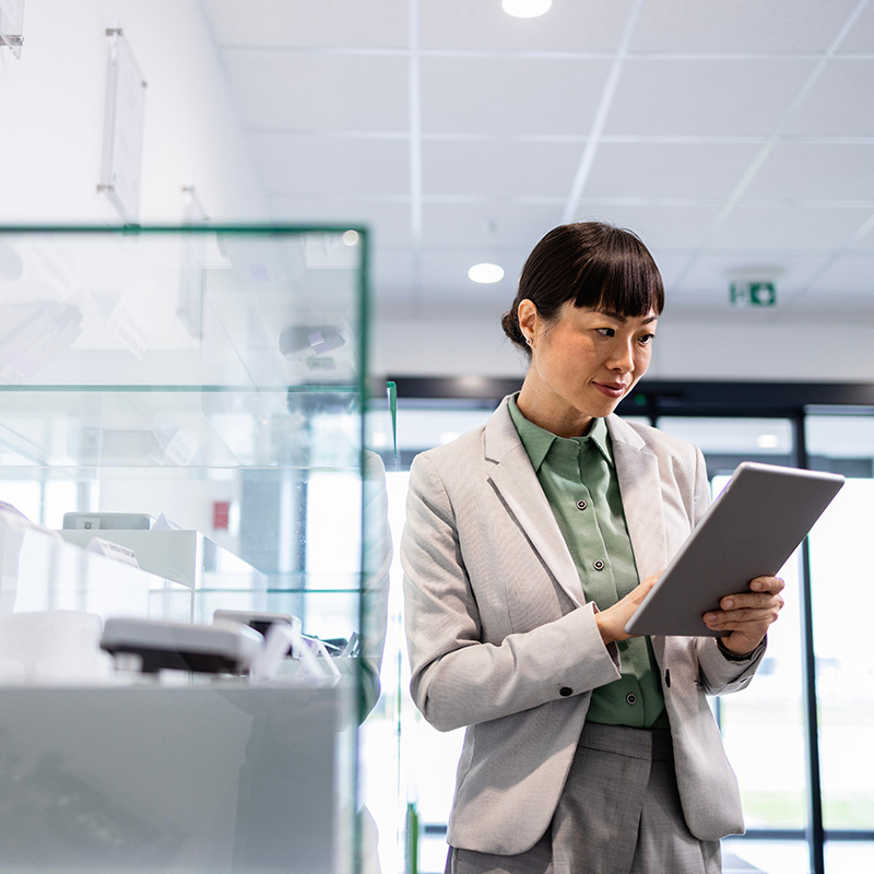 A woman in business attire is looking at a digital tablet in a modern, minimalist space. She appears to be reviewing information or data.