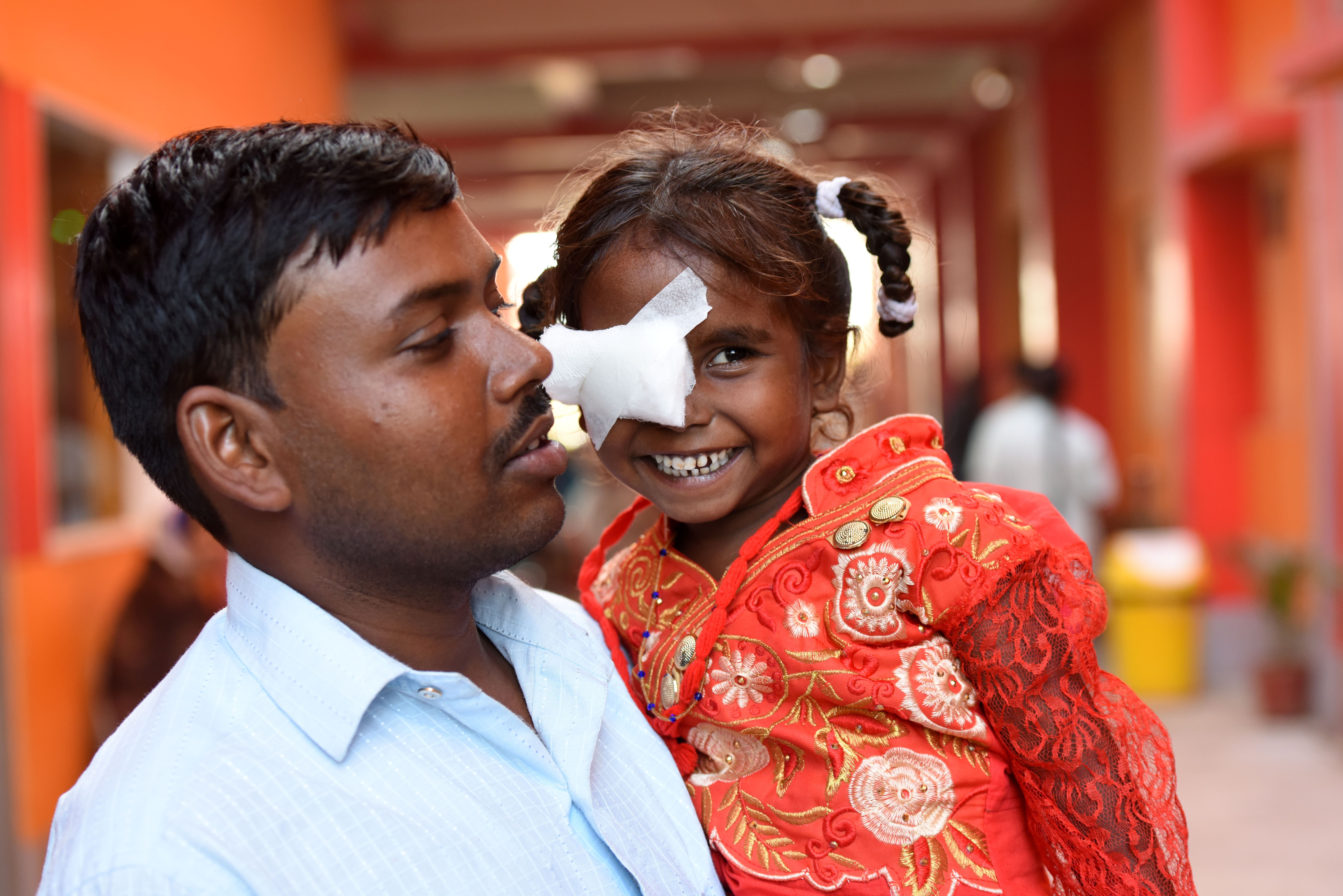 Man holding a little girl who is smiling and has one eye bandaged after surgery