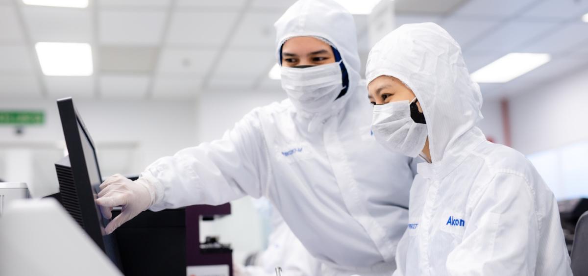 Lab employees in protective clothing looking at computer screen