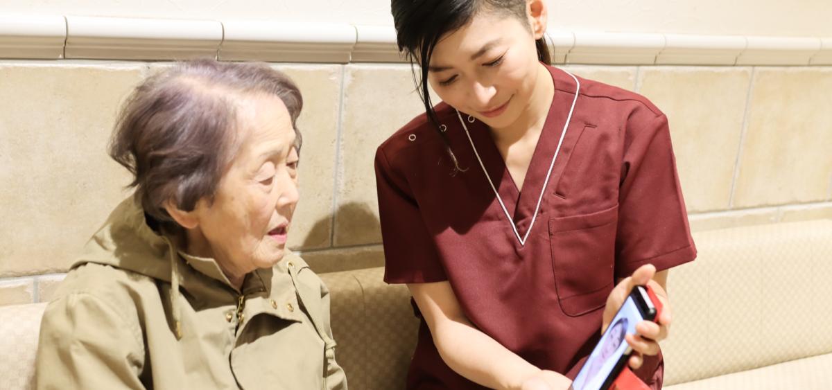 Young woman holds a phone up for an older woman who is on a video call with a medical professional