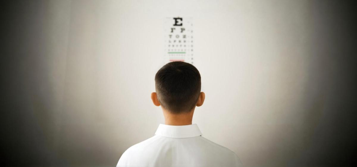 Man in a white shirt is looking at an eye chart.