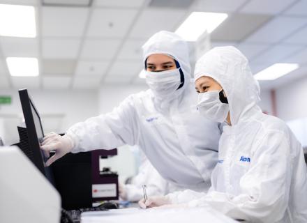 Lab employees in protective clothing looking at computer screen