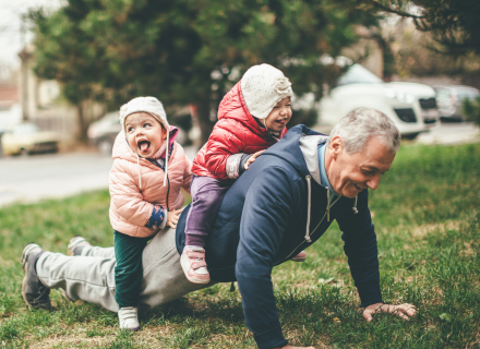 Older man with 2 small children riding on his back.