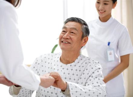 Smiling man in hospital gown grasping hands with doctor with nurse smiling behind him