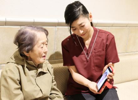 Young woman holds a phone up for an older woman who is on a video call with a medical professional
