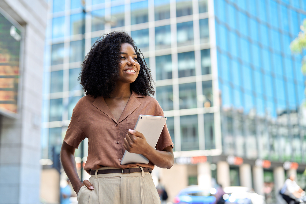 A young Black woman holding a tablet, looking upwards.