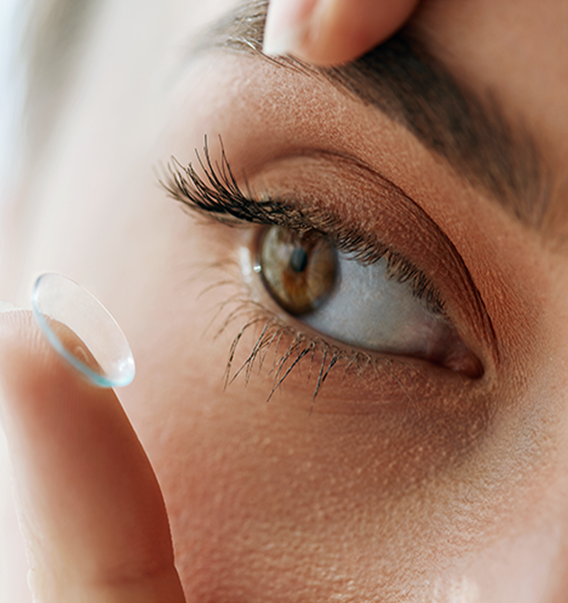 Close-up of a person’s eye as they prepare to insert a contact lens using their index finger
