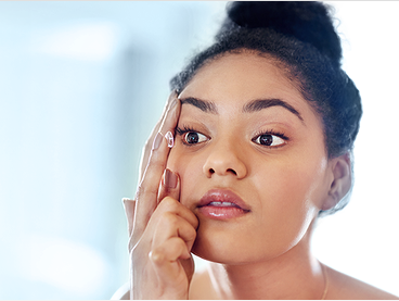Woman applying a contact lens to her right eye while looking into a mirror
