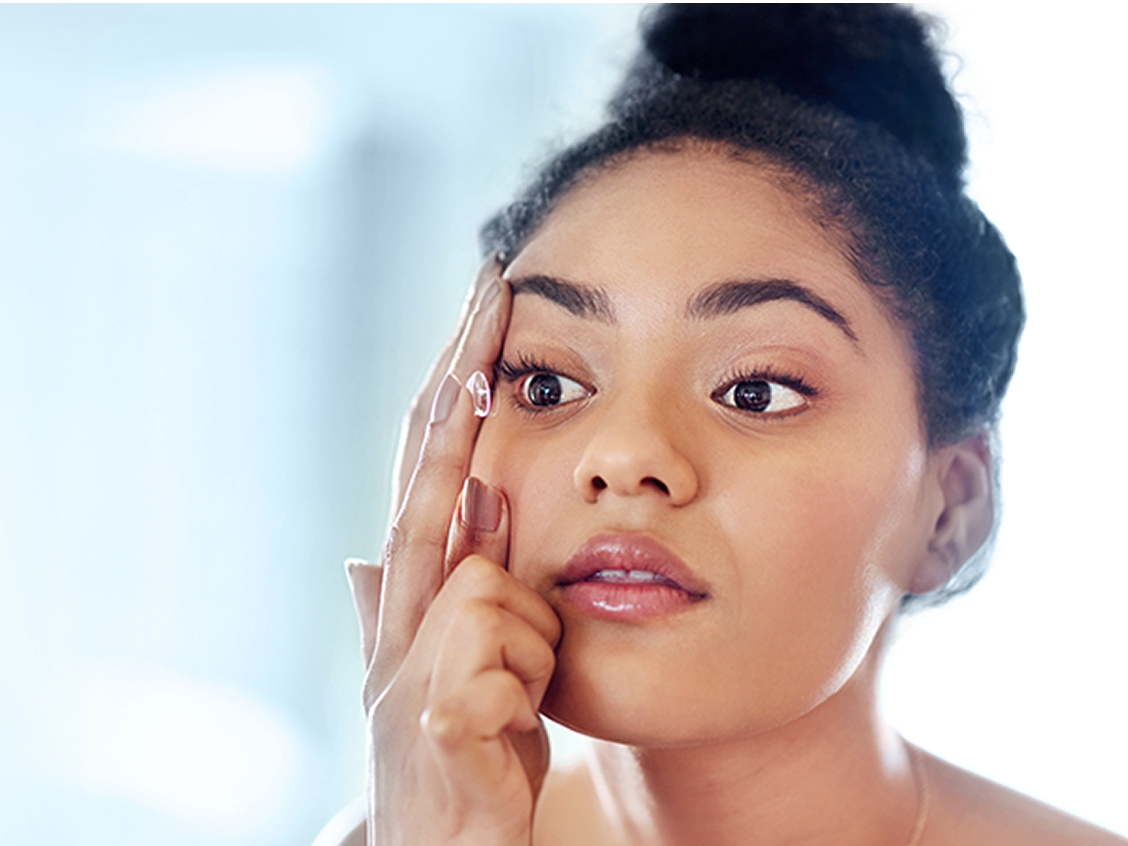 Woman applying a contact lens to her right eye while looking into a mirror