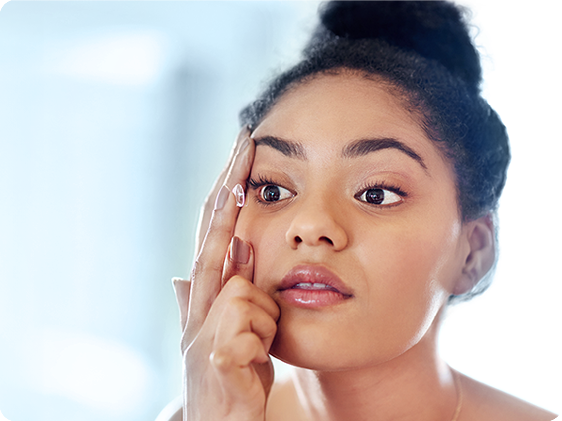 Woman applying a contact lens to her right eye while looking into a mirror