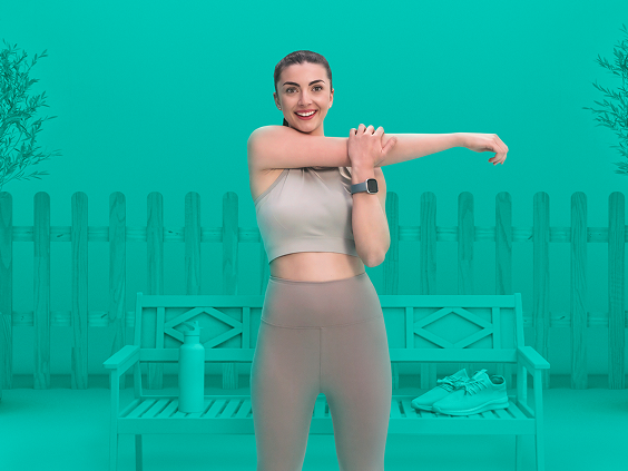 Woman in athletic wear stretching her arm in front of a bench with a water bottle and sneakers, set against a teal background with potted trees and a fence