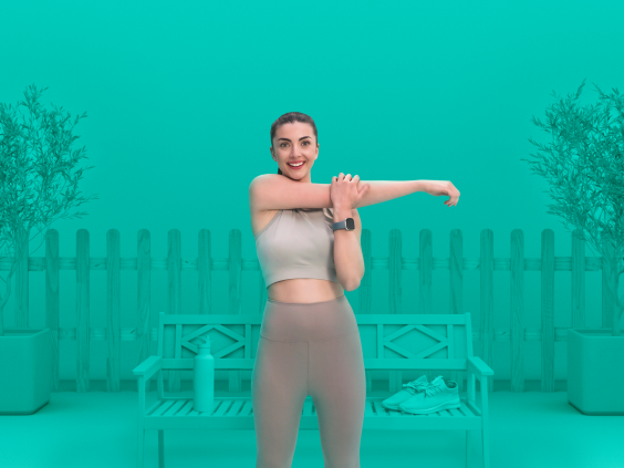 Woman in athletic wear stretching her arm in front of a bench with a water bottle and sneakers, set against a teal background with potted trees and a fence