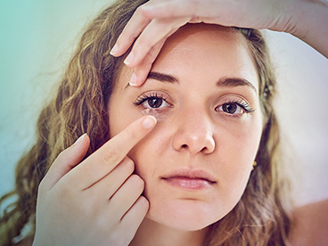 Gros plan sur une femme qui place une lentille de contact dans son œil, en tenant délicatement sa paupière supérieure tout en guidant la lentille avec son doigt.